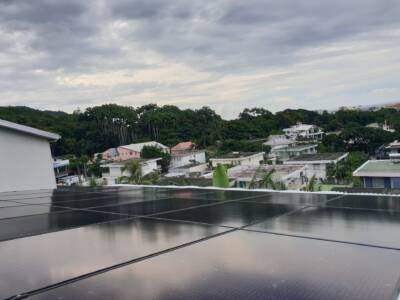Panneaux solaires noirs sur un toit à La Réunion, ville en arrière-plan avec arbres et palmiers