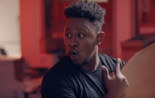 Homme portant un t-shirt noir dans un studio avec des murs rouges et un microphone.