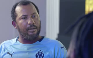 Un homme portant un maillot de football bleu de l'Olympique de Marseille avec logo Puma et une barbe noire sur fond neutre.