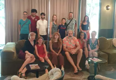 Image d'un groupe de personnes posant dans un salon avec des rideaux beige et un canapé sombre.