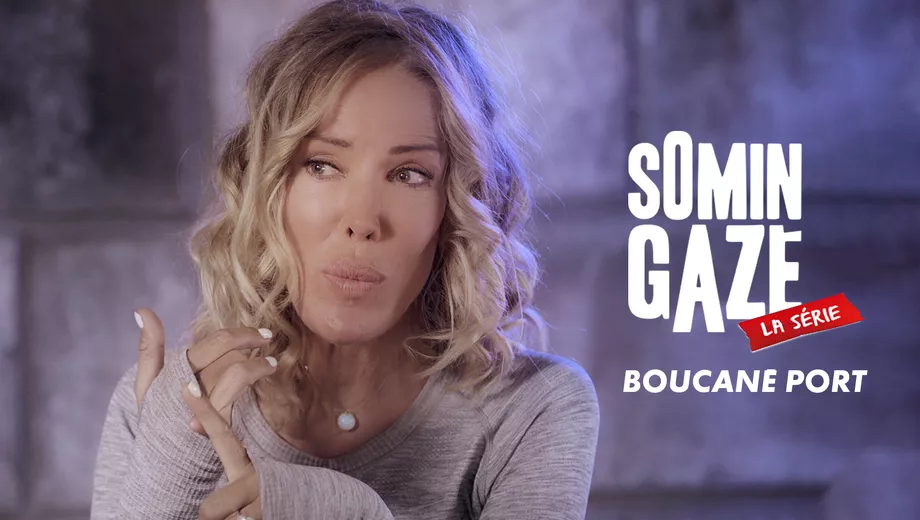 Femme aux cheveux blonds bouclés portant un pull gris et une chaîne à perle blanche, en réflexion sur fond flou gris. Text...