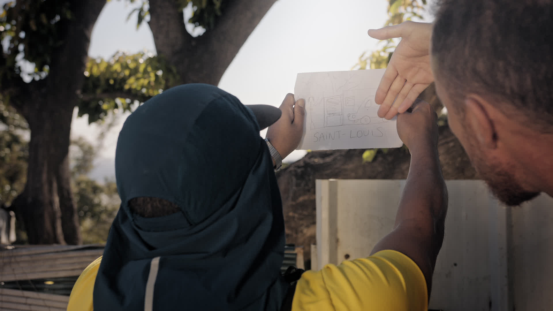 Deux femmes, l'une portant un hijab noir, regardent ensemble un dessin représentant Saint-Louis sur une feuille de papier....