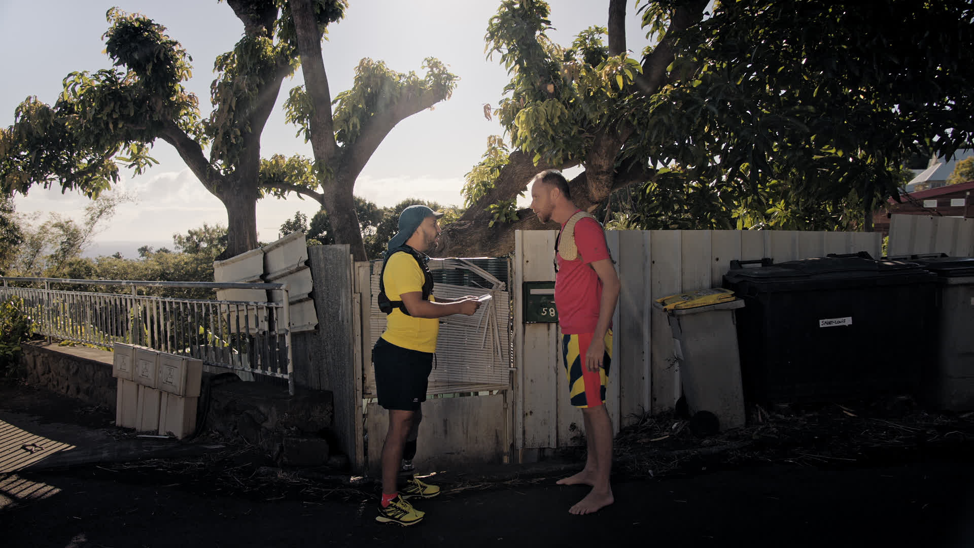 Deux hommes en short et tee-shirt, l'un portant un t-shirt jaune et des chaussures de sport jaunes, l'autre un t-shirt rou...