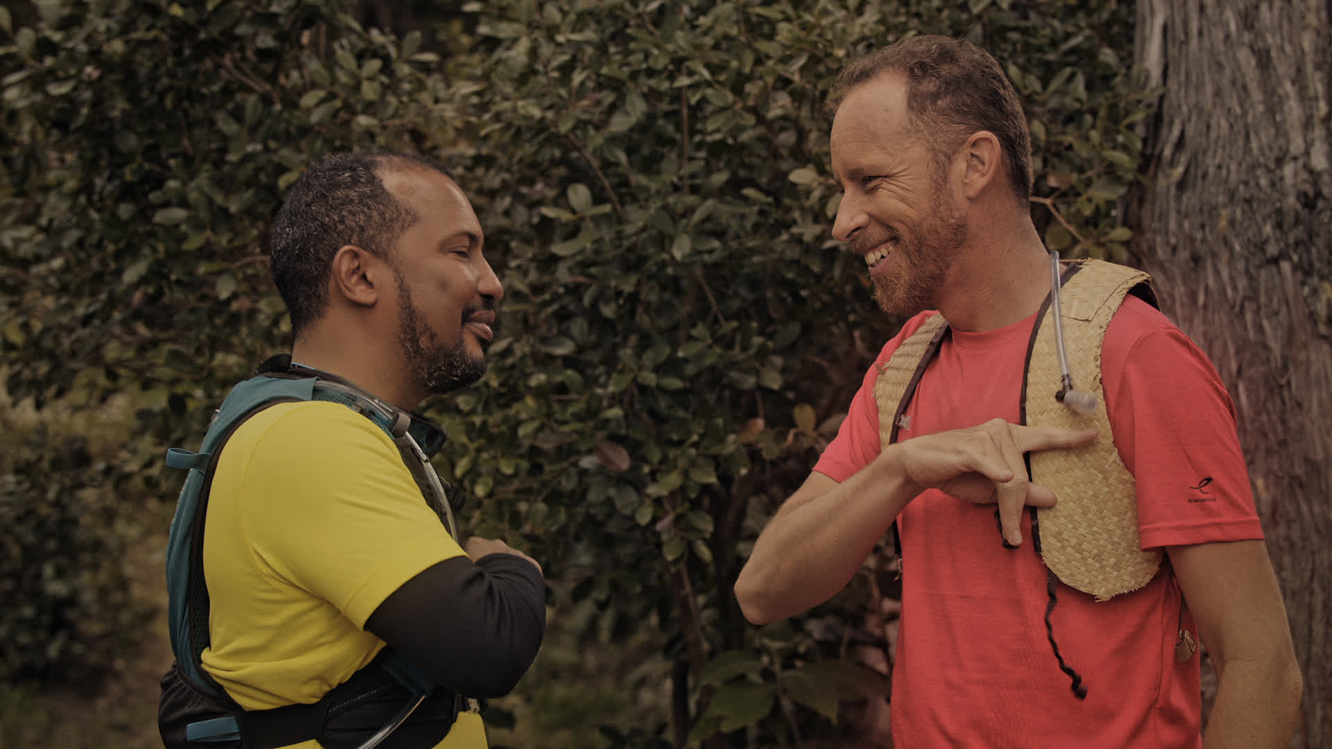 Deux hommes en pleine discussion dans un environnement forestier avec des sacs à dos de couleur bleu et rose - La Réunion