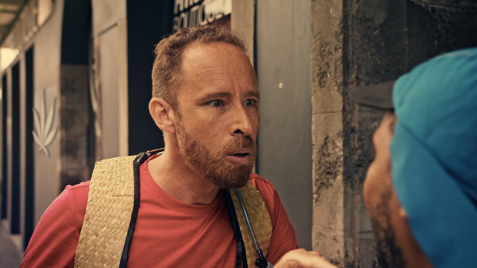 Homme barbu portant un tee-shirt orange dans une rue urbaine à La Réunion.