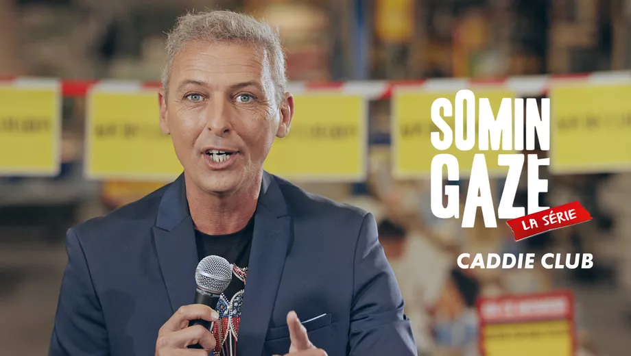 Homme en costume tenant un microphone avec des pancartes jaunes 'SOMIN GAZE' et 'LA SÉRIE CADDIE CLUB' à l'arrière.